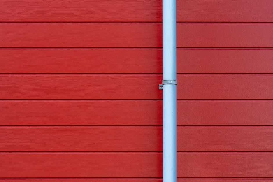 Descente de gouttière blanche sur une façade rouge