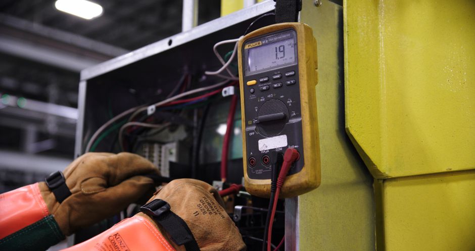 Électricien mesurant une tension avec un multimètre sur un coffret de commande
