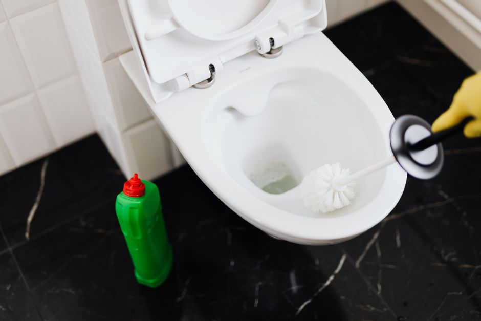 Main gantée nettoyant une cuvette de WC à la brosse
