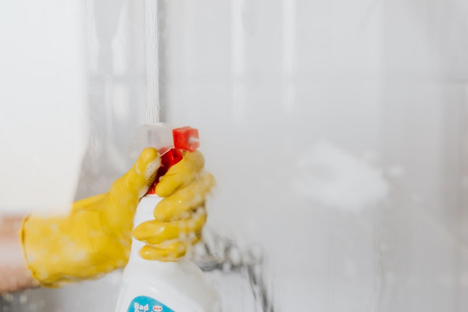 Main gantée vaporisant un produit sur une paroi de douche