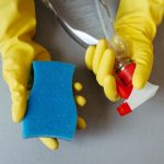 Mains gantées tenant une éponge et un vaporisateur de produit ménager