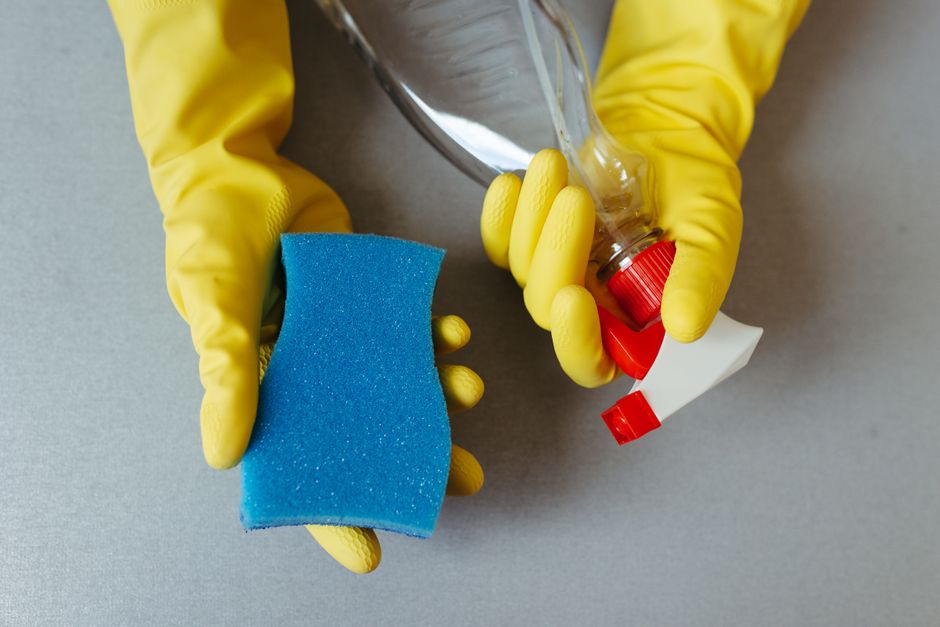 Mains gantées tenant une éponge et un vaporisateur de produit ménager