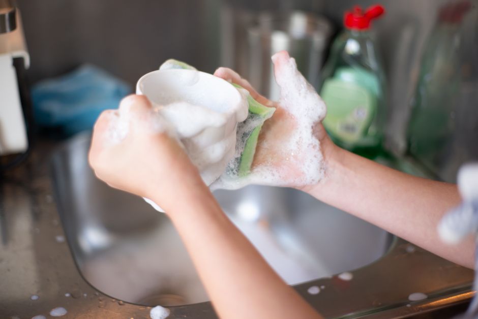 Mains lavant une tasse dans un évier avec de la mousse
